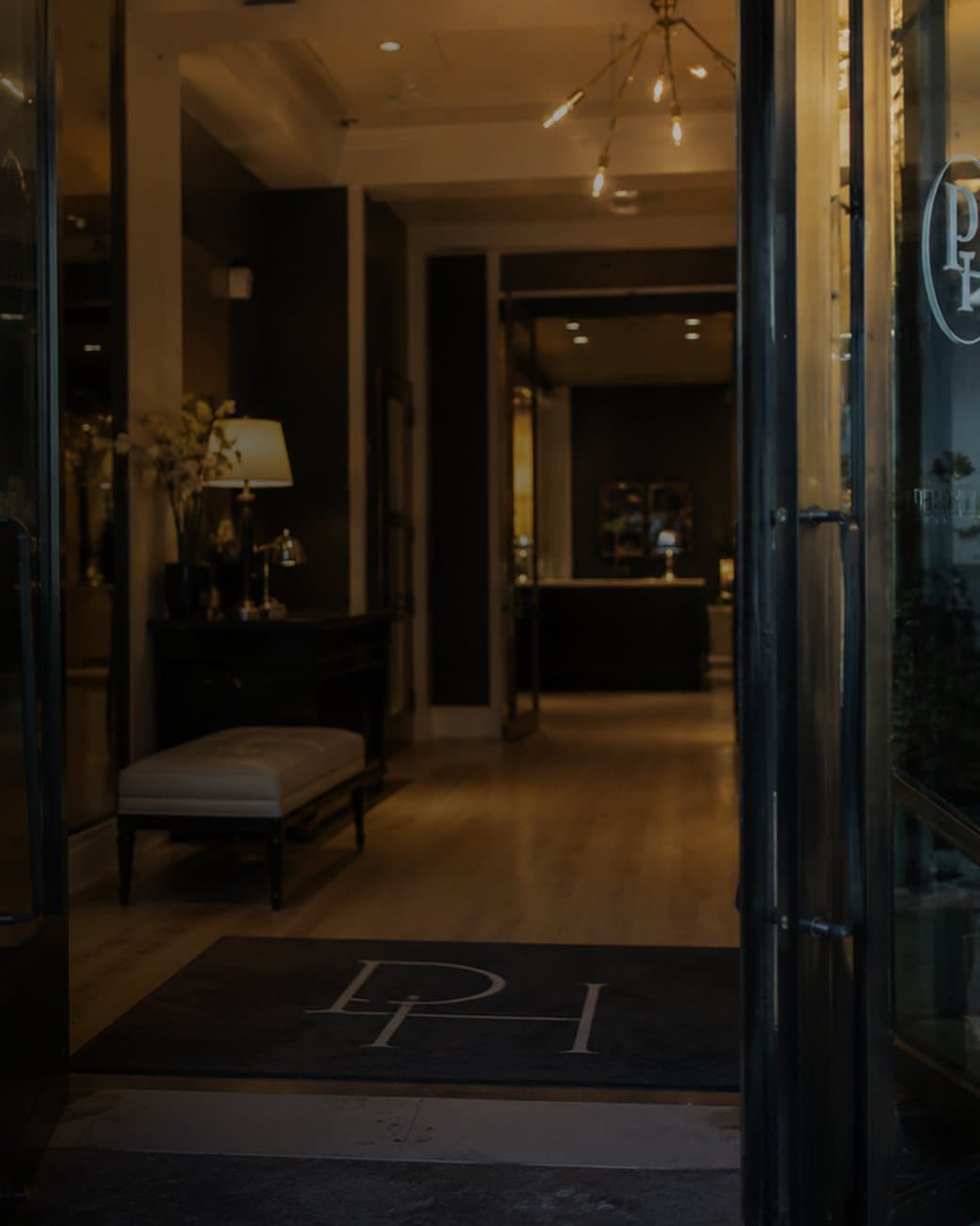 The open front doors of a hotel at dusk, looking through to the lit reception